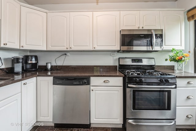 kitchen featuring dark tile patterned flooring, stainless steel appliances, white cabinets, and dark stone countertops