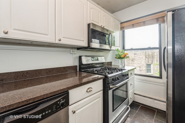 kitchen with white cabinets, dark tile patterned flooring, a baseboard radiator, and stainless steel appliances