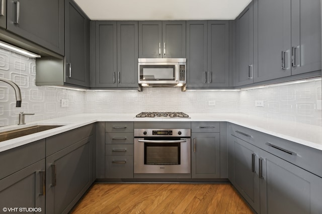 kitchen with stainless steel appliances, gray cabinetry, and light hardwood / wood-style floors