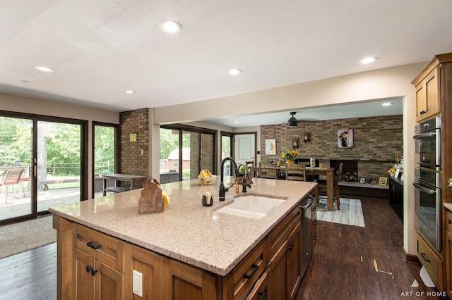 kitchen featuring sink, dark wood-type flooring, light stone countertops, and an island with sink