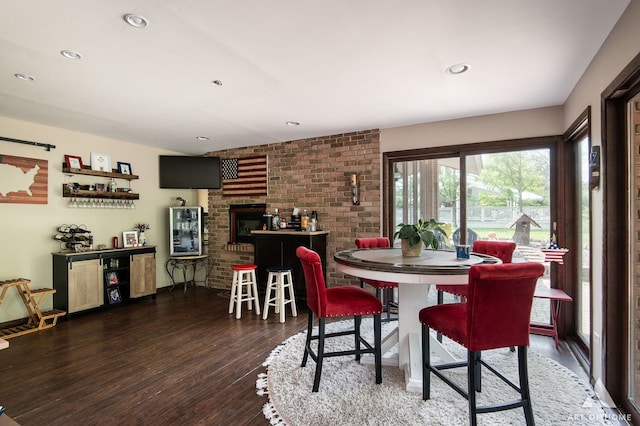 dining area with hardwood / wood-style flooring, a fireplace, and brick wall