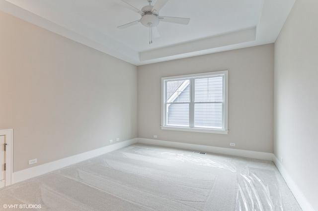 spare room featuring ceiling fan, light carpet, and a tray ceiling