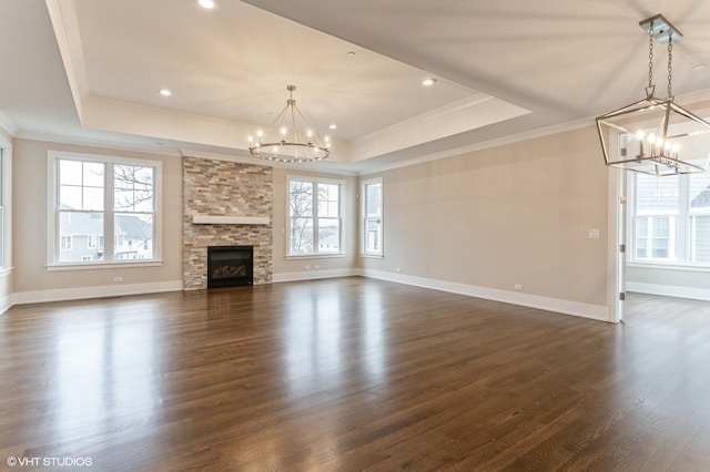 unfurnished living room featuring a raised ceiling, dark wood-type flooring, an inviting chandelier, and a fireplace