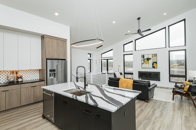 kitchen with appliances with stainless steel finishes, light wood-type flooring, an island with sink, and sink