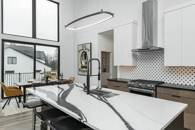 kitchen featuring wall chimney range hood, a kitchen island with sink, wood-type flooring, white cabinets, and high end range