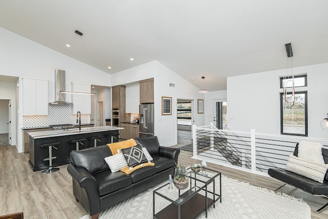 living room featuring light wood-type flooring, sink, a chandelier, and high vaulted ceiling