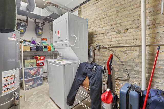clothes washing area featuring water heater, stacked washer / drying machine, laundry area, and brick wall