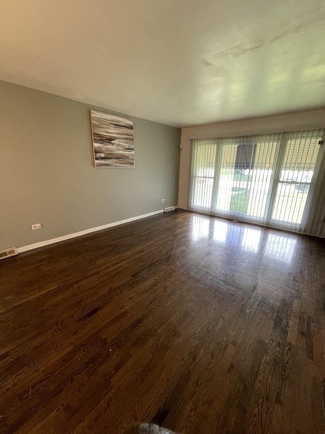 empty room featuring dark wood-style flooring, visible vents, and baseboards