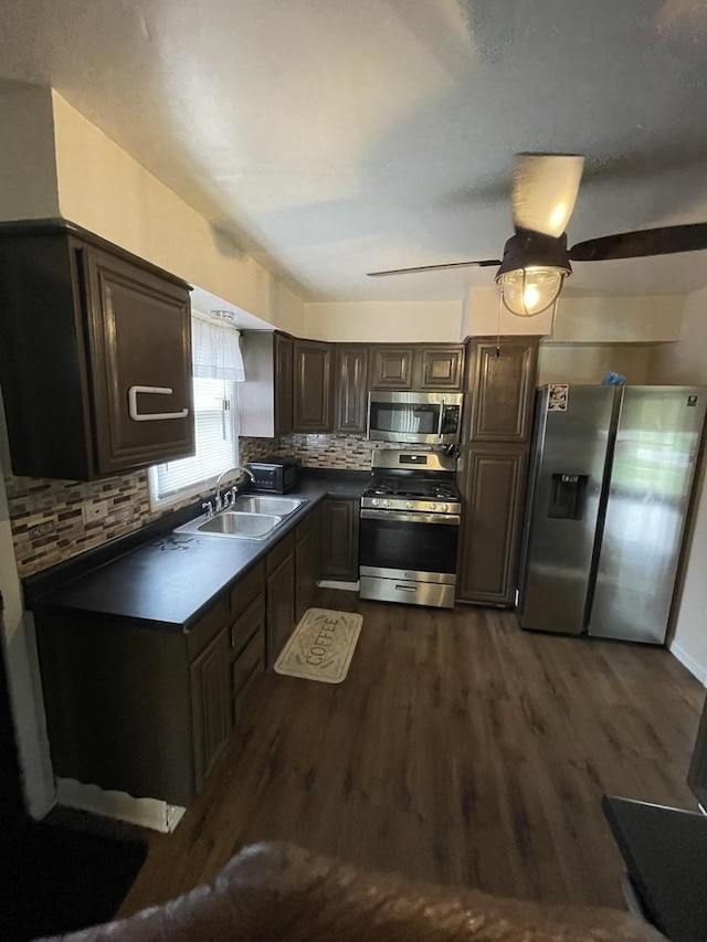 kitchen featuring dark countertops, appliances with stainless steel finishes, dark wood-type flooring, a sink, and backsplash