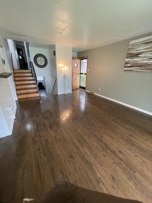 unfurnished living room featuring stairway, dark wood-style flooring, and baseboards