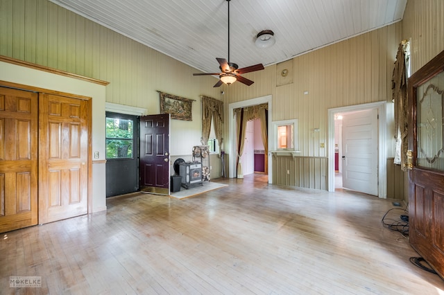 interior space with ceiling fan, light wood-type flooring, a high ceiling, and a wood stove