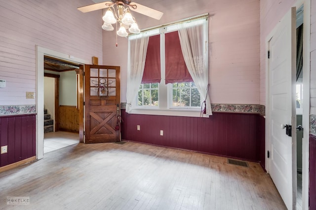 unfurnished room featuring visible vents, a wainscoted wall, wood walls, stairs, and wood finished floors