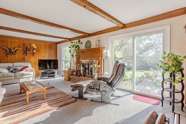 carpeted living room featuring beamed ceiling, a brick fireplace, and wood walls