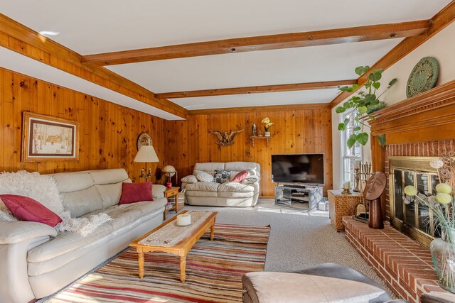 living room with beam ceiling, wooden walls, a brick fireplace, and carpet flooring