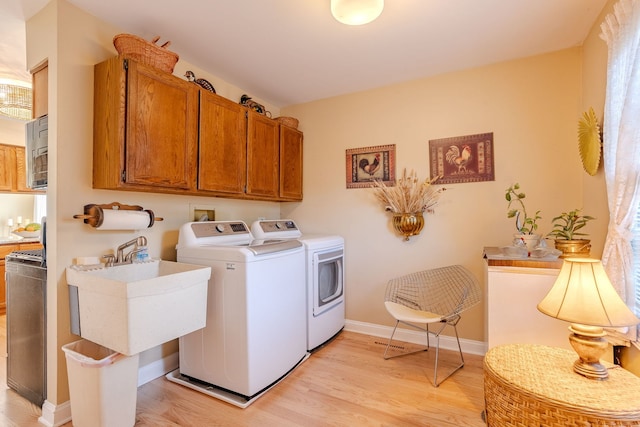 washroom with light hardwood / wood-style floors, sink, washer and clothes dryer, and cabinets