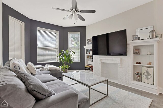 living room featuring ceiling fan, wood-type flooring, and a brick fireplace