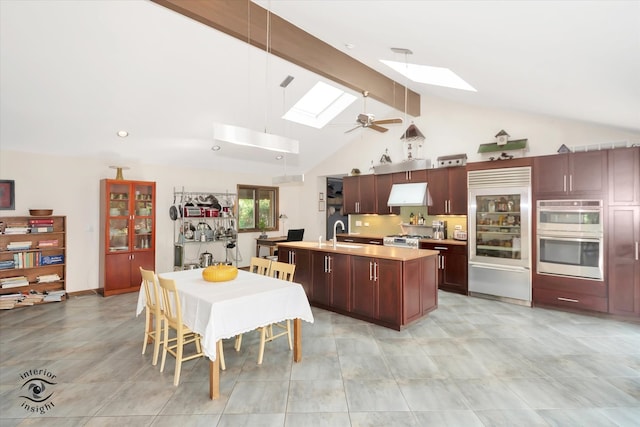 kitchen with beamed ceiling, a skylight, ceiling fan, appliances with stainless steel finishes, and a center island with sink