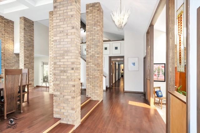 hall with dark wood-type flooring, decorative columns, and an inviting chandelier