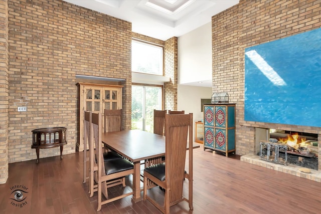 dining room with brick wall, a high ceiling, dark hardwood / wood-style flooring, and a multi sided fireplace