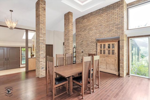 dining space featuring a towering ceiling, dark wood-type flooring, a chandelier, and brick wall