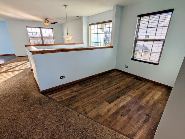 empty room with plenty of natural light, ceiling fan, and dark wood-type flooring