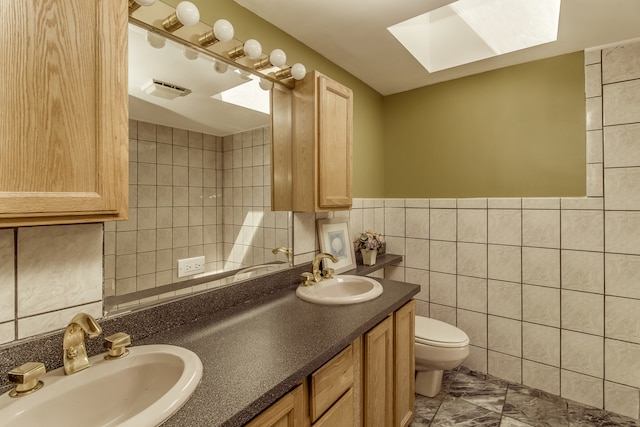 bathroom featuring vanity, tile walls, toilet, and a skylight