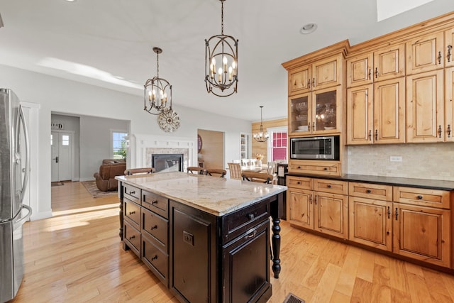 kitchen featuring a fireplace, light wood-style flooring, decorative backsplash, appliances with stainless steel finishes, and a chandelier