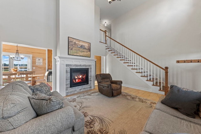 living room featuring a stone fireplace, high vaulted ceiling, hardwood / wood-style flooring, and a chandelier