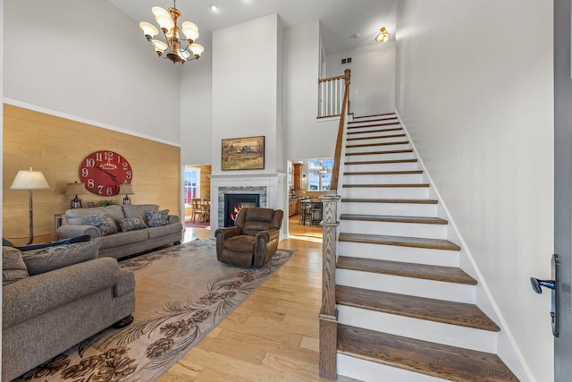 living room with stairway, a high ceiling, an inviting chandelier, a stone fireplace, and wood finished floors