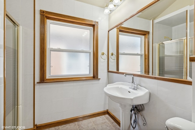 bathroom with a shower with door, toilet, tile patterned floors, and tile walls