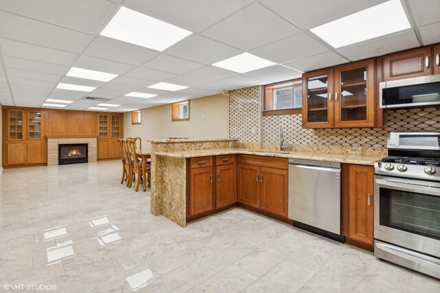 kitchen with a drop ceiling, appliances with stainless steel finishes, sink, a fireplace, and kitchen peninsula