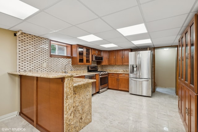 kitchen with appliances with stainless steel finishes, tasteful backsplash, light stone counters, a drop ceiling, and kitchen peninsula