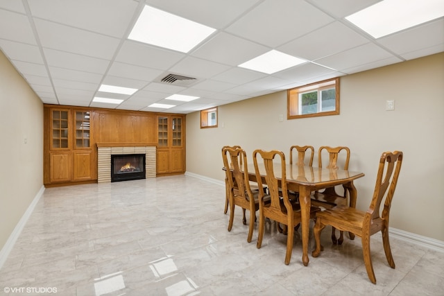 dining area featuring light tile patterned flooring, a paneled ceiling, and a fireplace