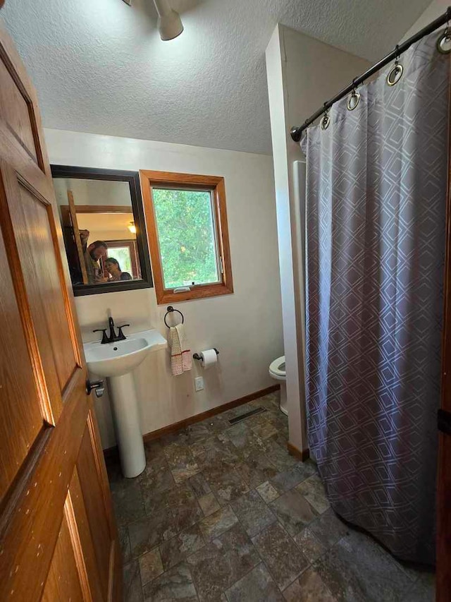 bathroom with curtained shower, a textured ceiling, toilet, and sink