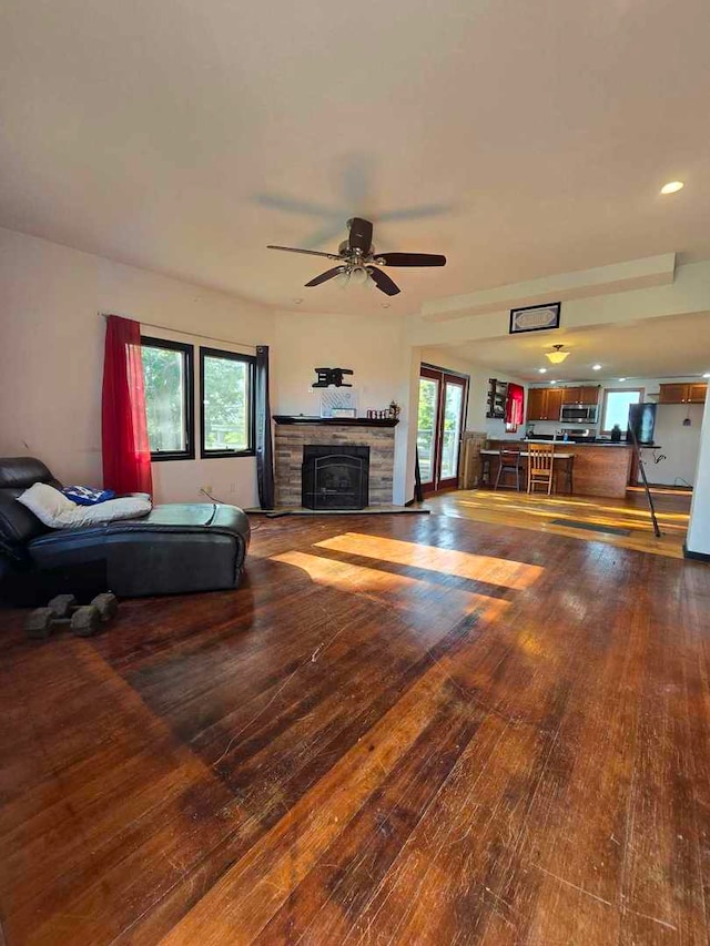 living room featuring hardwood / wood-style flooring, ceiling fan, and a stone fireplace