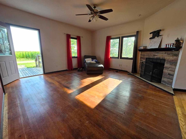 unfurnished living room featuring a stone fireplace, dark hardwood / wood-style flooring, and ceiling fan