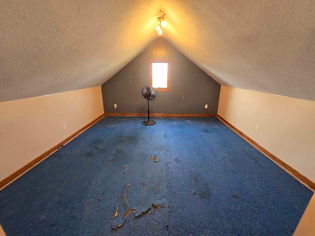 additional living space featuring lofted ceiling, a textured ceiling, and dark colored carpet