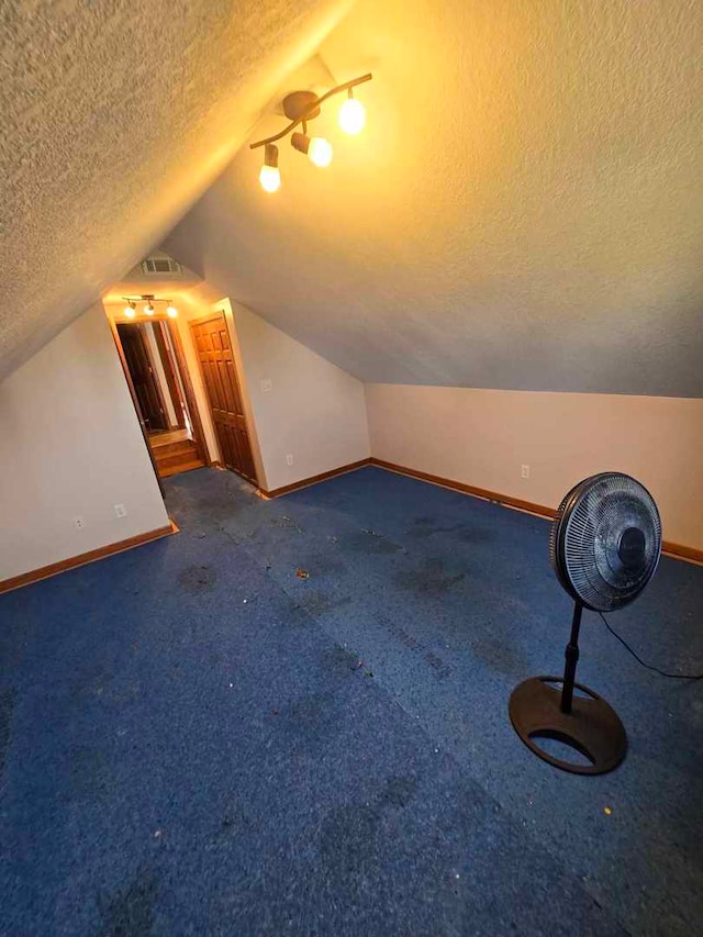 additional living space with lofted ceiling, a textured ceiling, and dark colored carpet