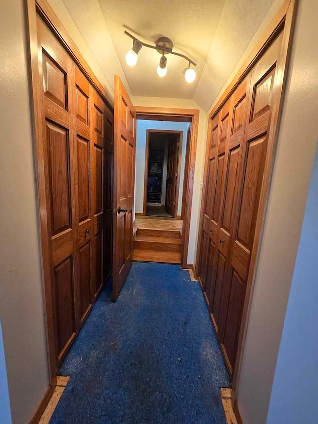 corridor with track lighting, vaulted ceiling, and dark carpet