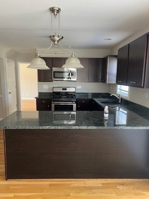 kitchen featuring sink, appliances with stainless steel finishes, hanging light fixtures, dark brown cabinetry, and dark stone counters