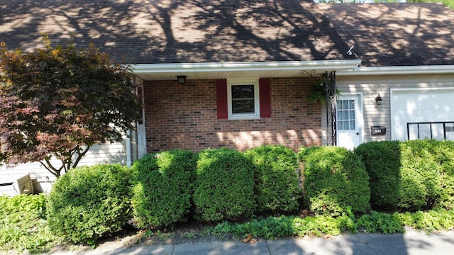 property entrance featuring roof with shingles and brick siding