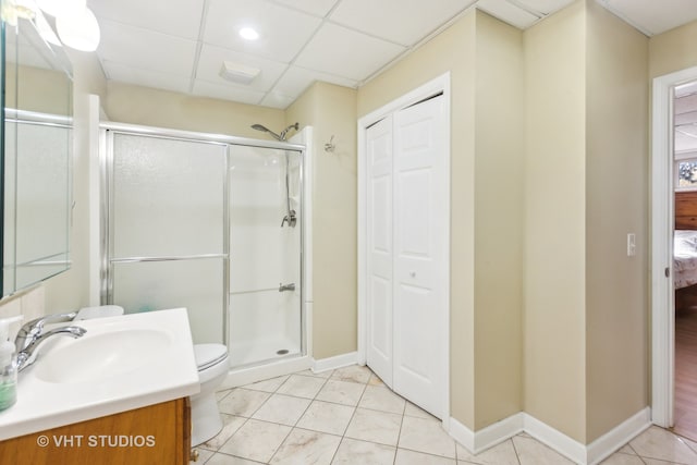 bathroom featuring a shower with door, tile patterned floors, toilet, vanity, and a paneled ceiling