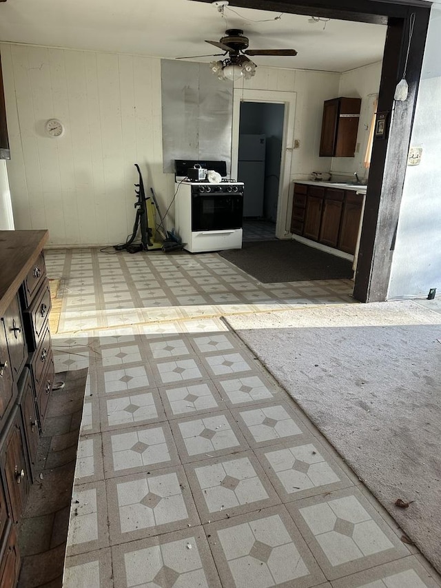 kitchen featuring dark brown cabinets, ceiling fan, light floors, gas range, and freestanding refrigerator