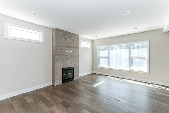 unfurnished living room with dark wood-style floors, a fireplace, baseboards, and a healthy amount of sunlight