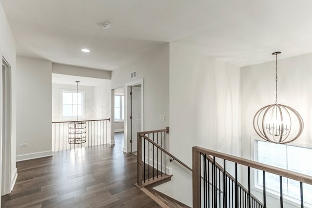 corridor featuring a chandelier, dark wood-type flooring, visible vents, an upstairs landing, and baseboards