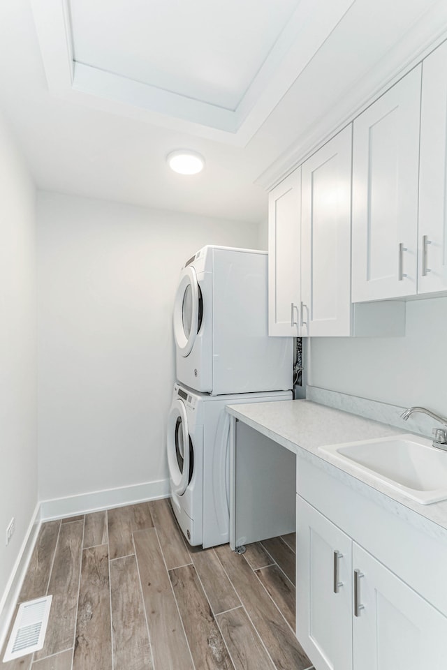 laundry area with wood finish floors, stacked washer / dryer, a sink, and visible vents