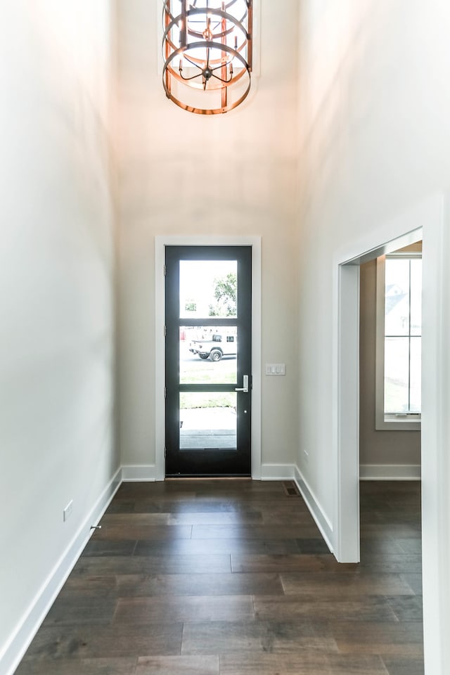 entryway with a towering ceiling, an inviting chandelier, baseboards, and dark wood-style flooring