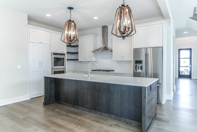 kitchen with appliances with stainless steel finishes, light countertops, white cabinetry, and wall chimney exhaust hood