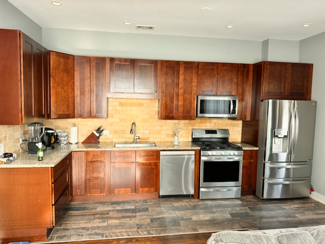 kitchen with appliances with stainless steel finishes, decorative backsplash, sink, and light stone countertops