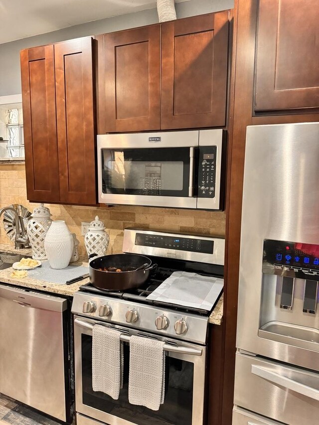 kitchen with appliances with stainless steel finishes, light stone countertops, and backsplash